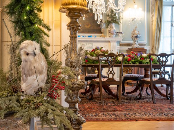 Fake owl sitting in evergreen boughs next to dining room table decorated for Christmas