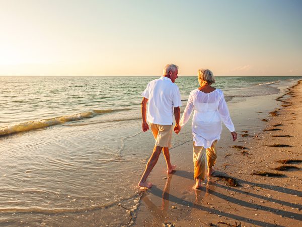 Happy senior man and woman old retired couple walking and holding hands on a beach at sunset