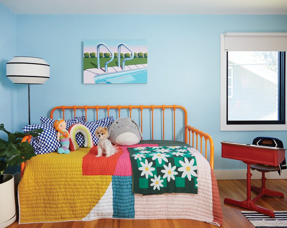 Child's bedroom with an orange iron daybed and colorful quilt next to a red vintage school desk
