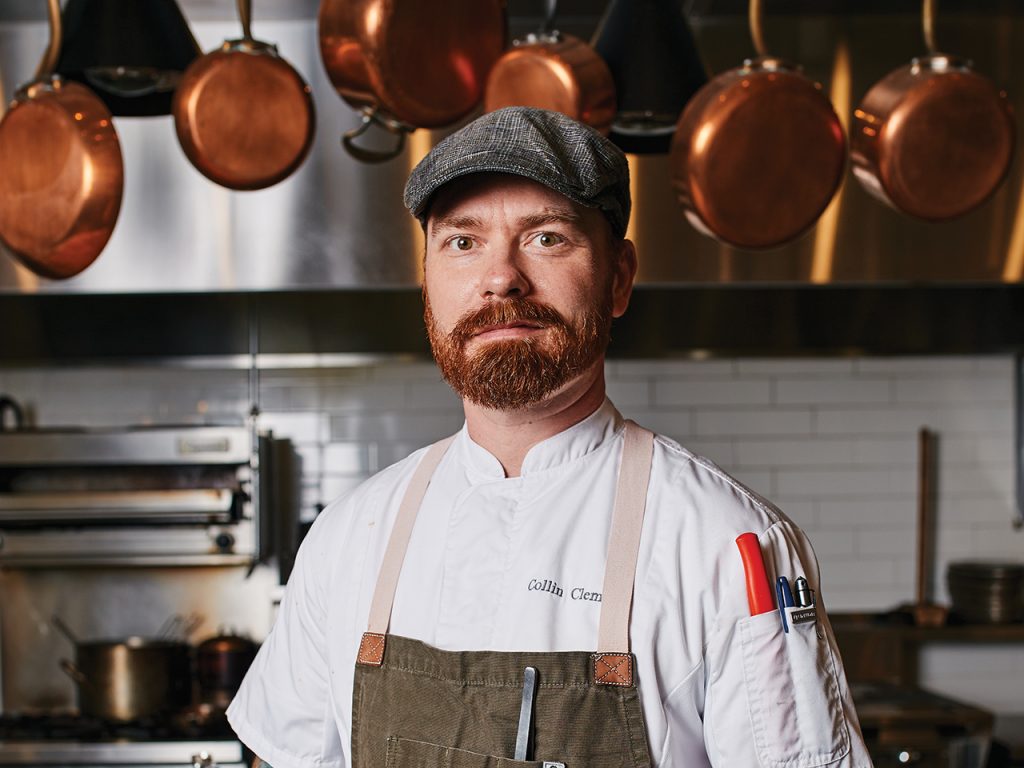 Chef standing in kitchen in front of hanging copper pots and pans