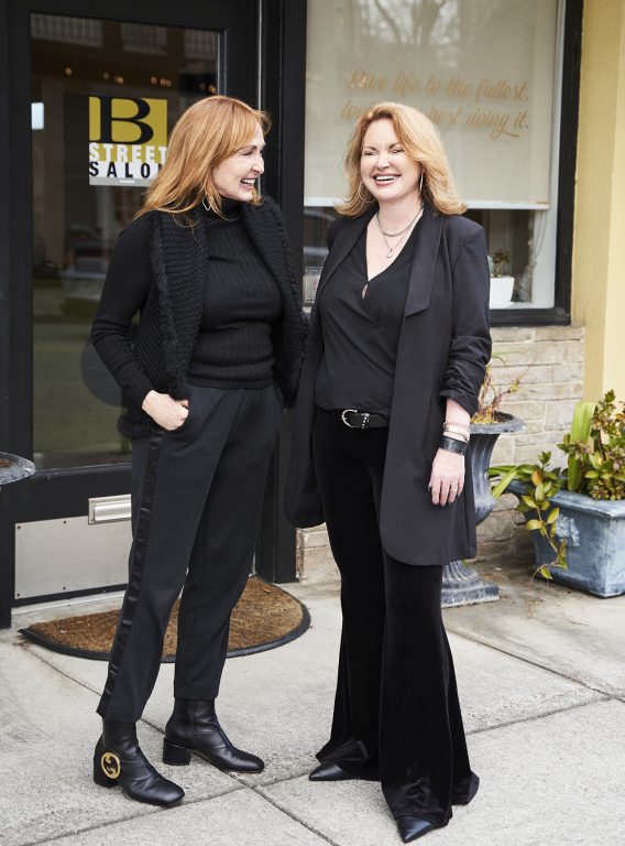 Two women dressed in black and standing outside a salon