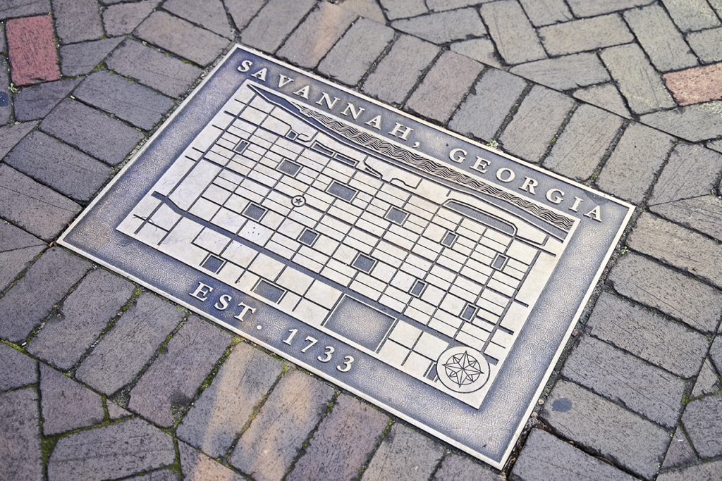 An emblem depicting Savannah's downtown squares and riverfront situated in a brick sidewalk
