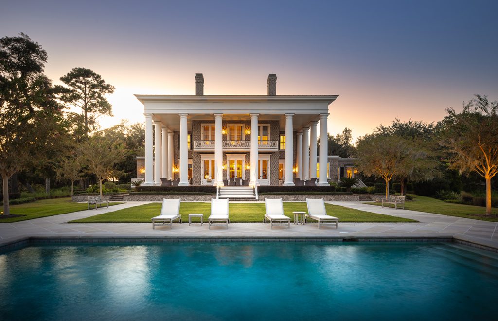 An in-ground pool in front of a huge house with columns