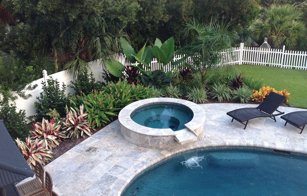 A pool and hot tub surrounded by lush landscaping and a white picket fence