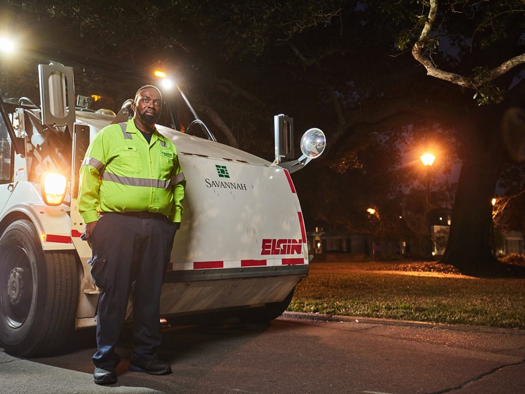 Man in reflective gear standing in front of a street sweeper