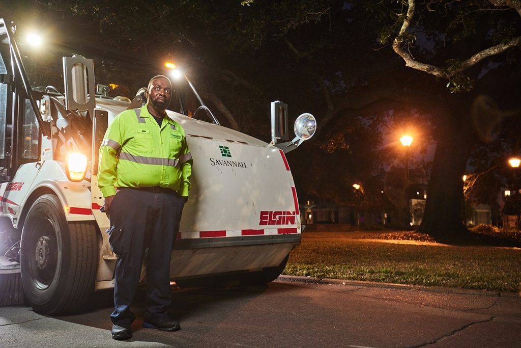 Man in reflective gear standing in front of a street sweeper