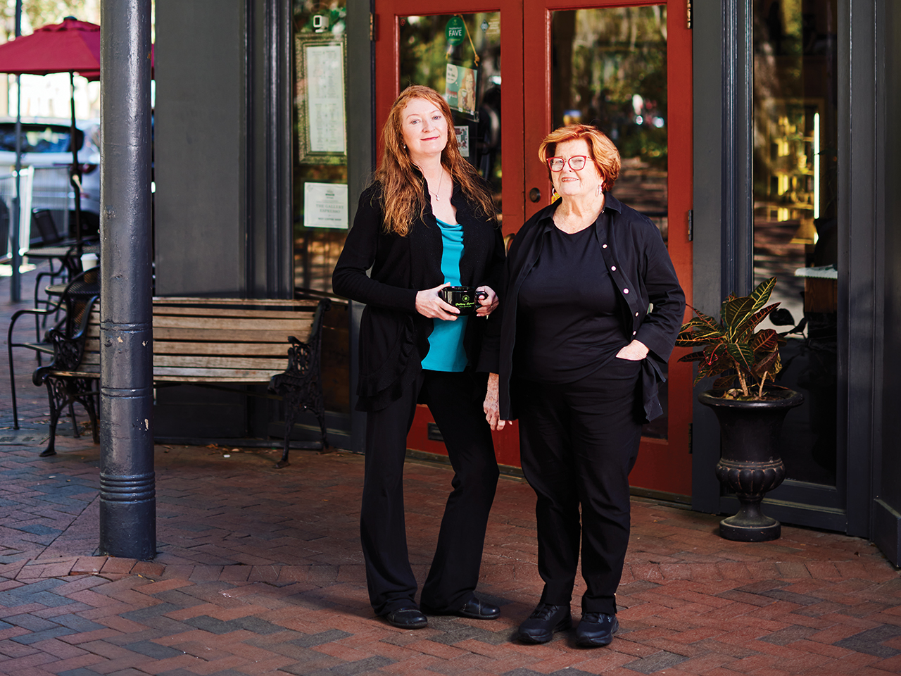 Two red-haired women standing in front of the doors to a coffee shop