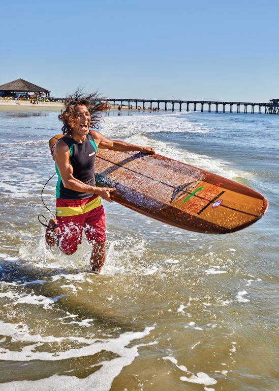 A smiling man holding a surfboard and running into the ocean