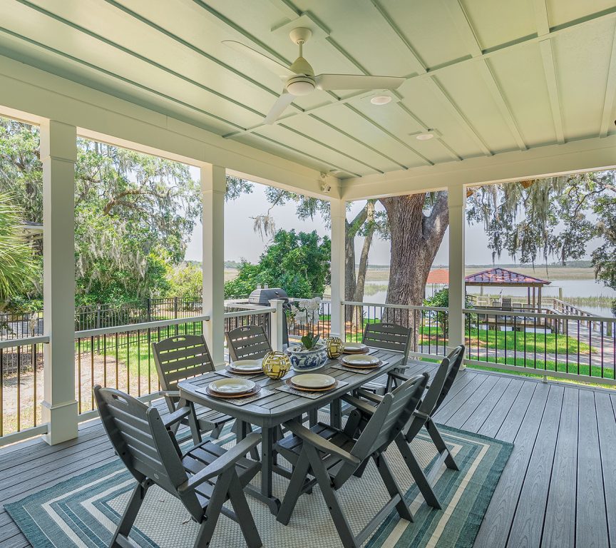 An outdoor dining table and chairs on a covered porch overlooking a river