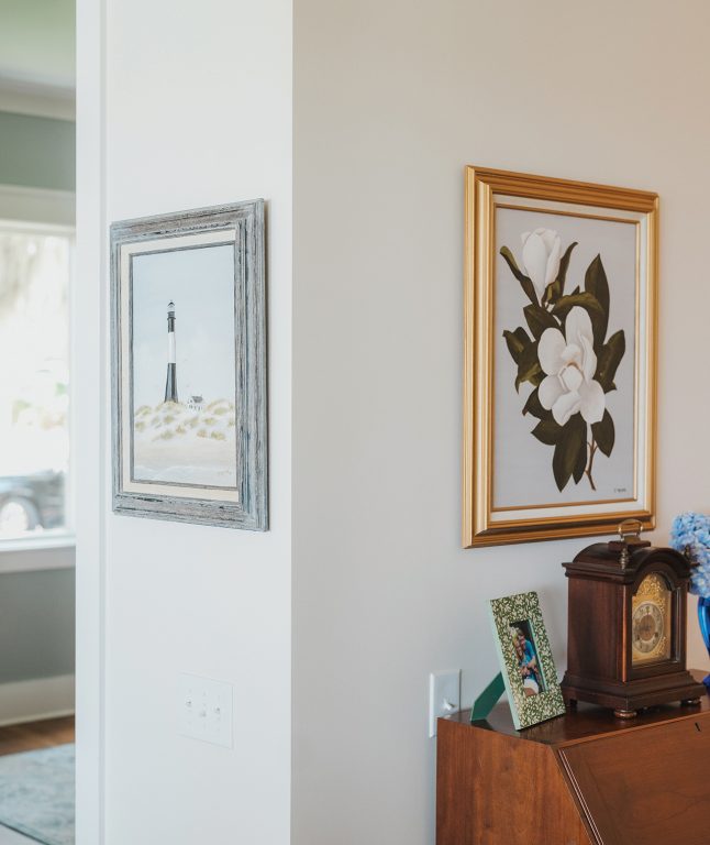 A painting of a lighthouse and a painting of a magnolia hanging on a wall