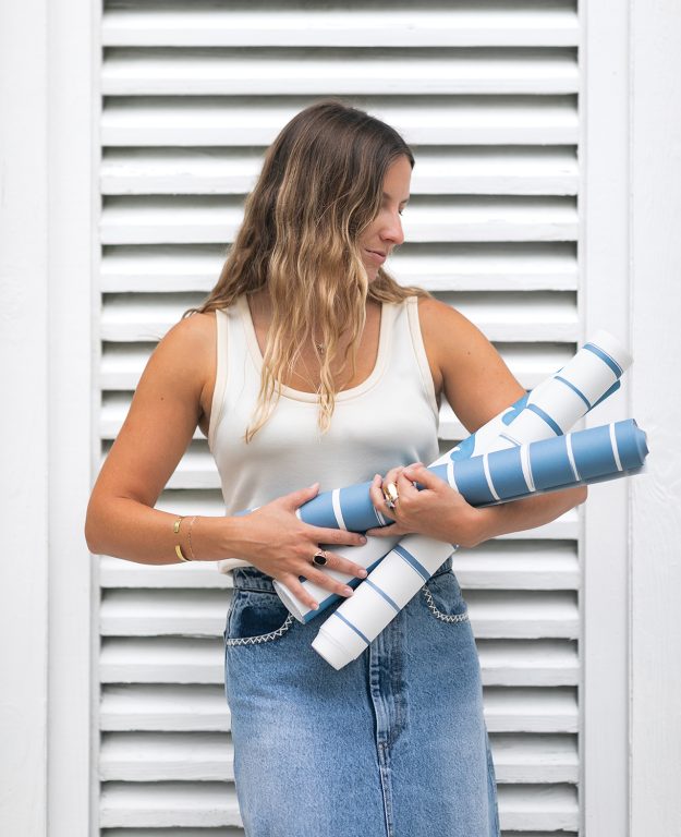 young woman standing in front of a white shutter and holding bolts of fabric