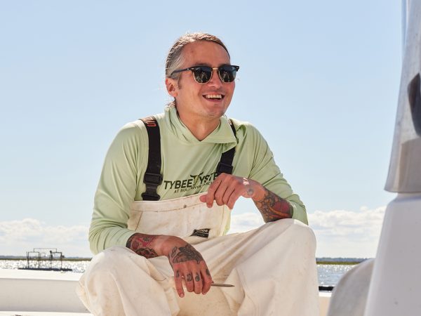 A man in white shirt and overalls sits on a boat, enjoying the serene waters.
