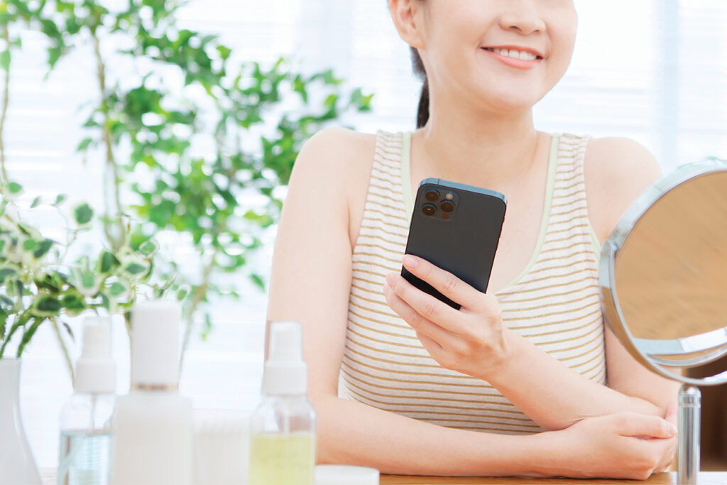 Woman holding a cellphone and looking into a makeup mirror