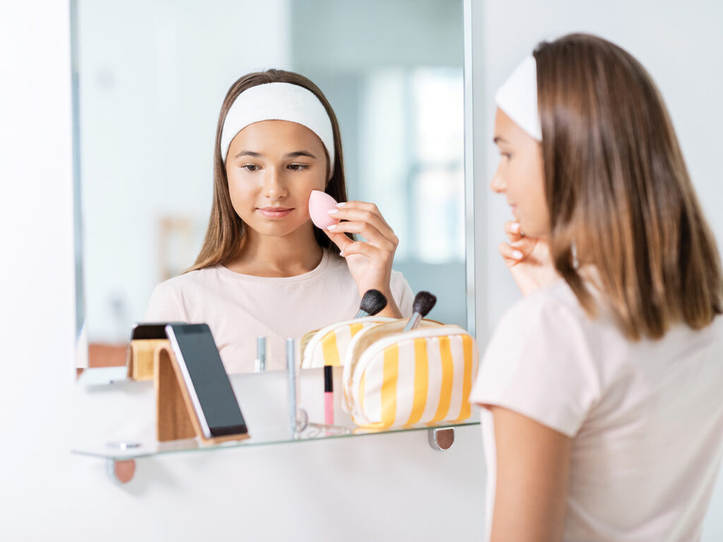 Teen girl putting makup on in front of a mirror