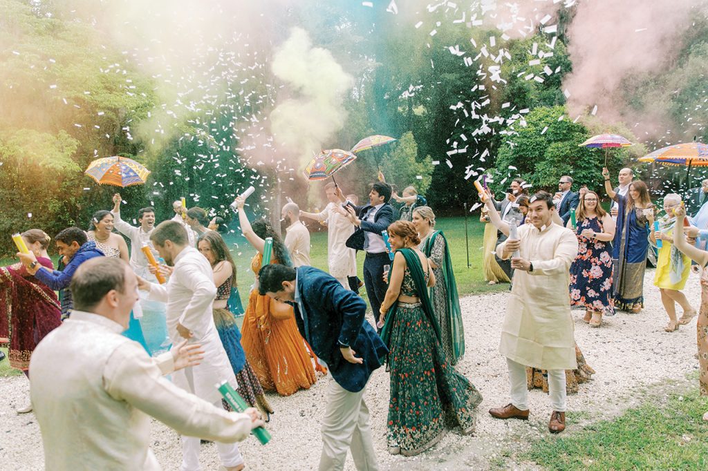Guests of an Indian wedding, holding up colorful umbrellas and throwing confetti