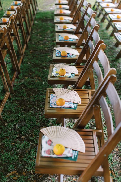 Wooden chairs lined up with an orange and hand-held fan on each seat