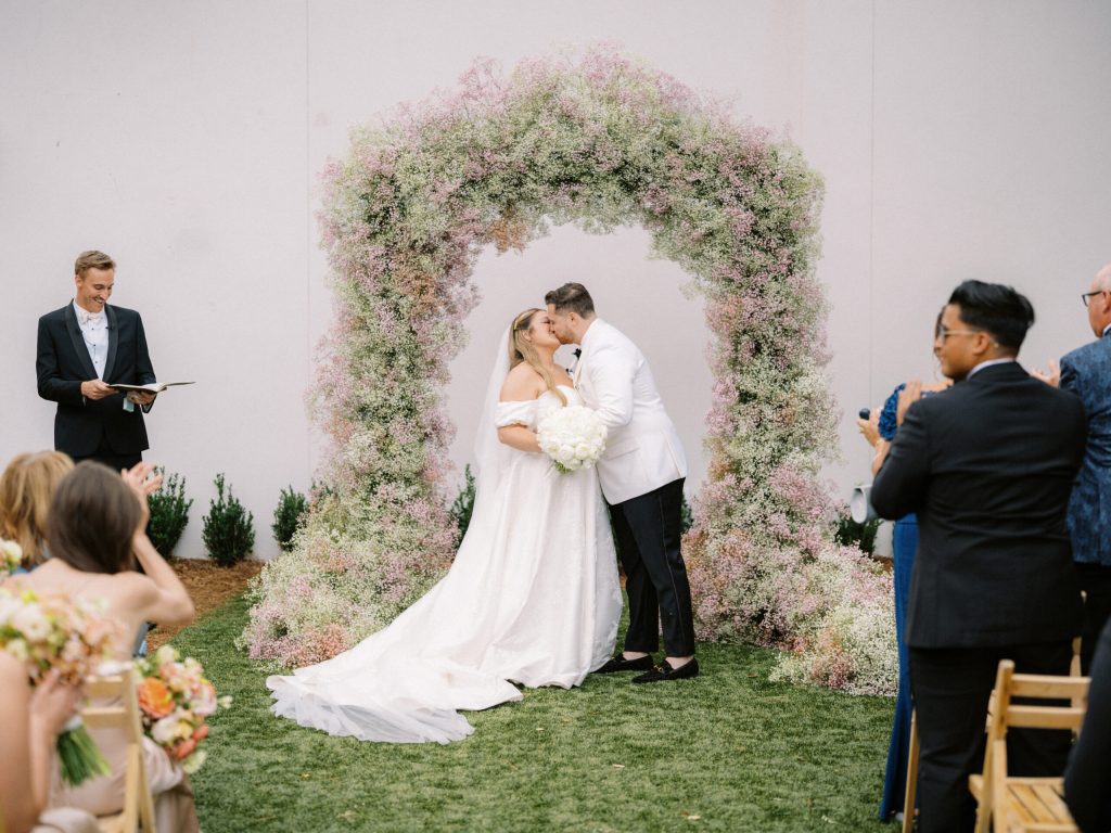 A bride and groom kissing under an arch of fresh flowers