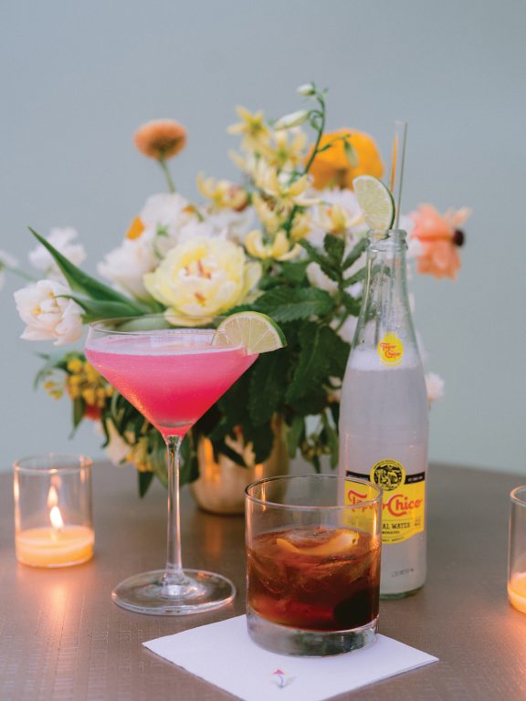 A pink martini sitting on a table, in front of a flower arrangement