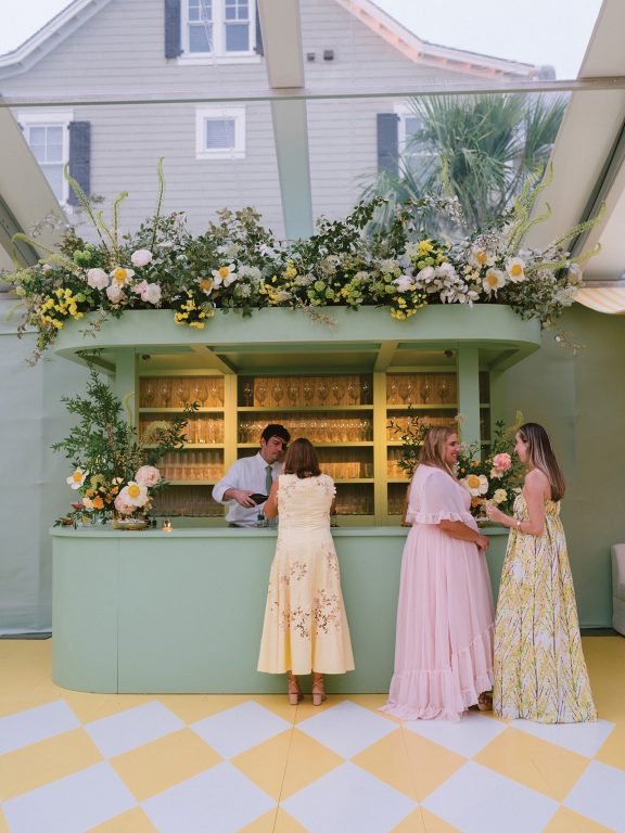 Women in bright pink and yellow dresses chatting at a bar