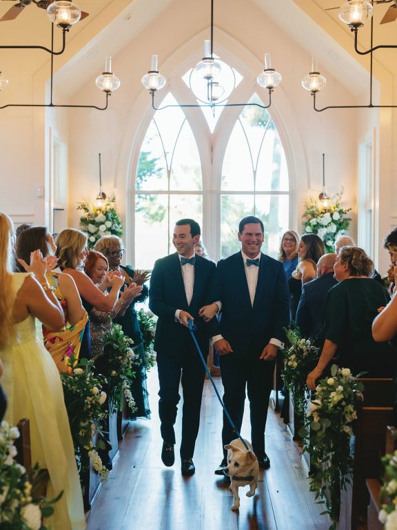 A newly-married couple walking down the church aisle with their dog