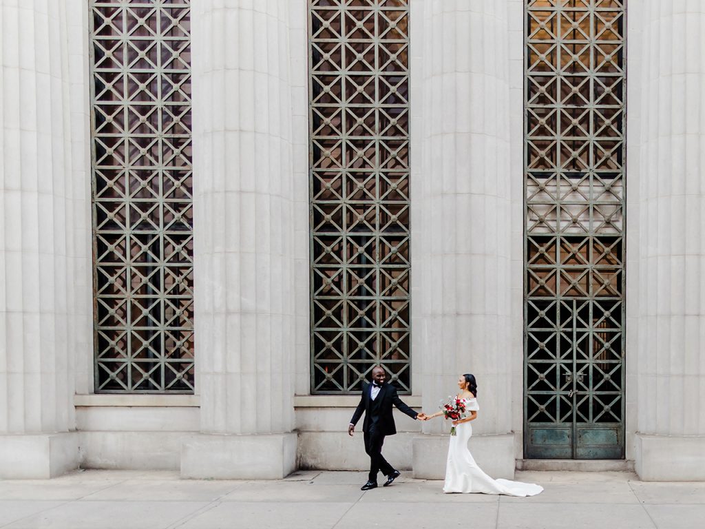 A bride and groom walking in front of giant concrete pillars