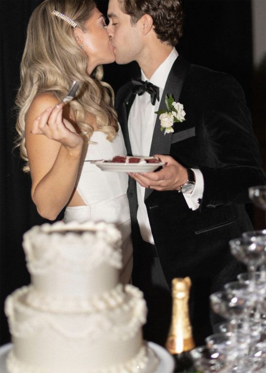 A bride and groom holding plates of wedding cake and kissing