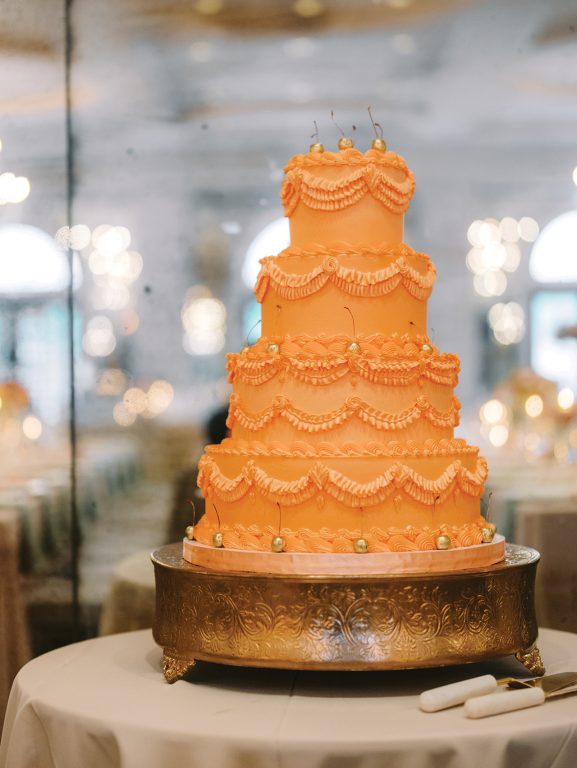 A four-tiered wedding cake with orange frosting