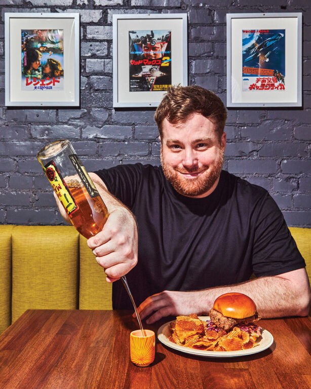 Man sitting at a table with a burger and fries and pouring a shot of alcohol