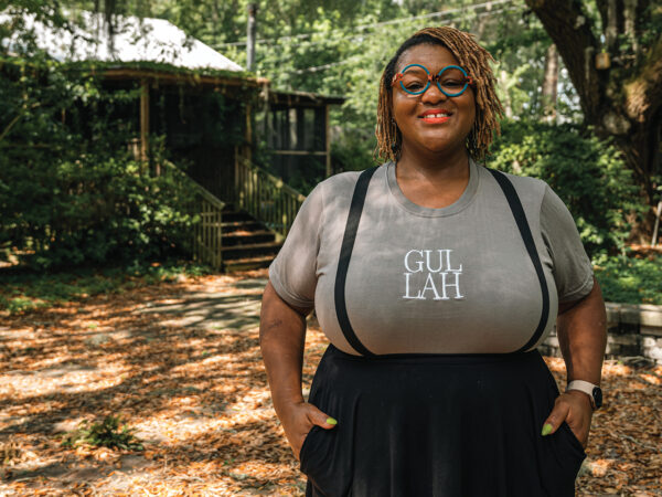 A black woman wearing glasses standing outside under a large oak tree