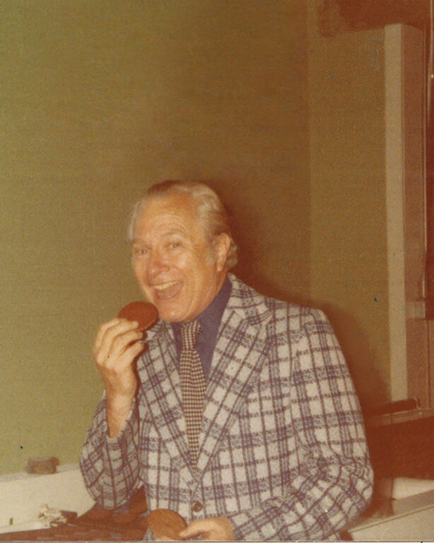 An old photo of a man smiling and eating a cookie