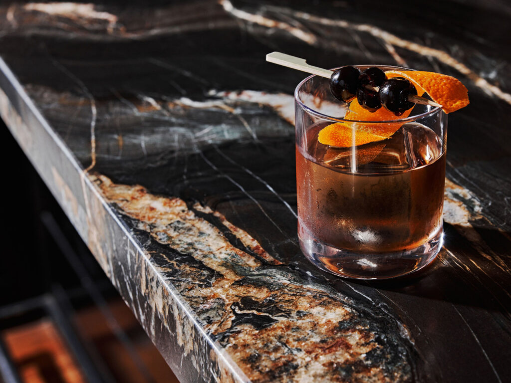 a Manhattan cocktail sitting on a dark marble bartop