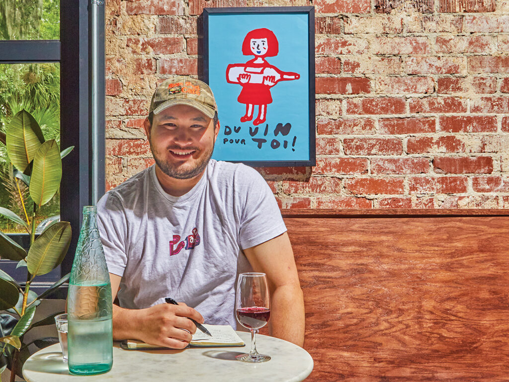 A man in a baseball cap sitting at a table with a pen, paper and glass of wine
