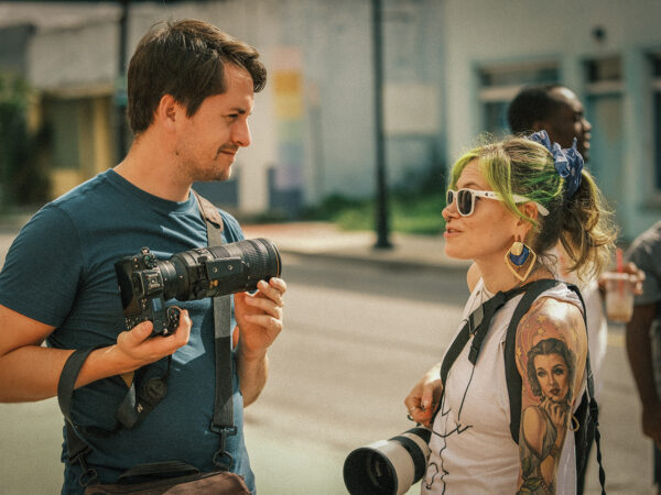 A man and a woman holding cameras talking to each other