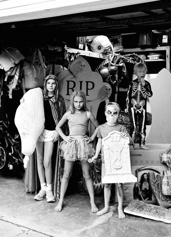 four kids dressed in halloween costumes standing in a garage full of halloween decorations