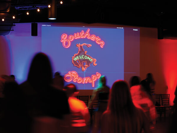 people line dancing on a dark dance floor with a welcome sign lit up in the background