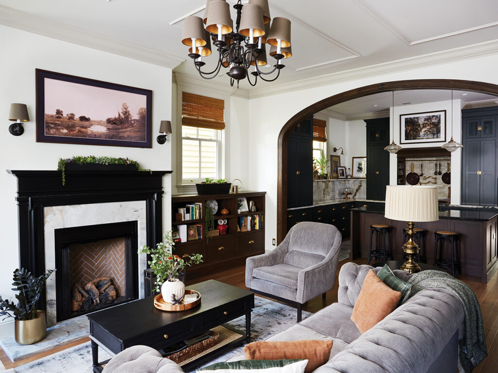 Living room with a turn-of-the-century fireplace mantel painted in Sherwin-Williams Tricorn Black and flanked by custom wood bookcases