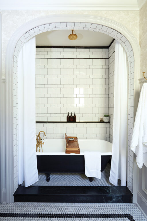 A clawfoot tub inside a bathroom nook with a curved entryway and alternating square and subway tile walls and penny tile floor
