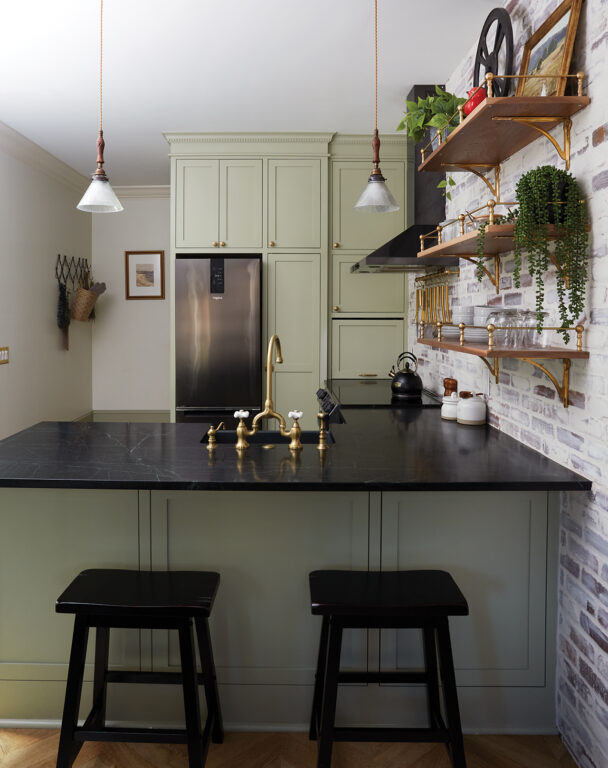 Kitchen with moss green cabinets, exposed brick wall and dark marble countertops
