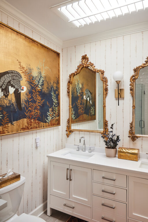 Bathroom with double vanity, two gold-framed mirrors and a large painting of a stork