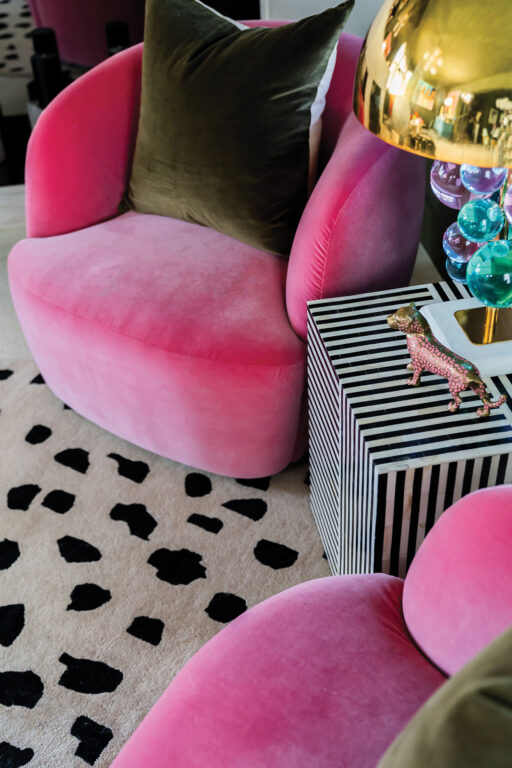 Hot pink living room chairs, white rug with black splotches and a black and white striped end table