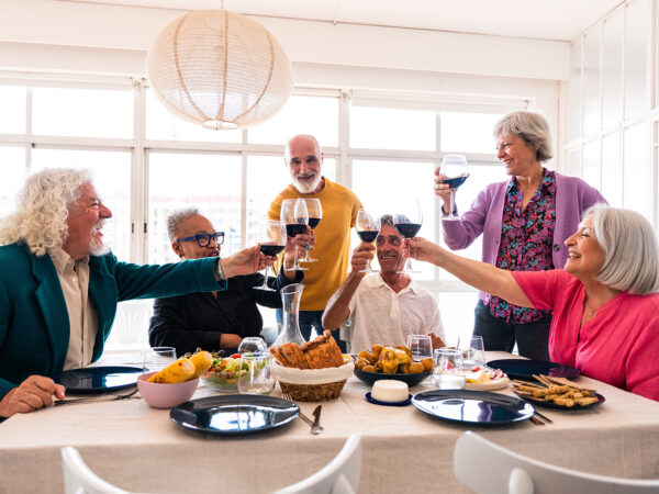 Senior citizens sitting around a dinner table holding up glasses of wine