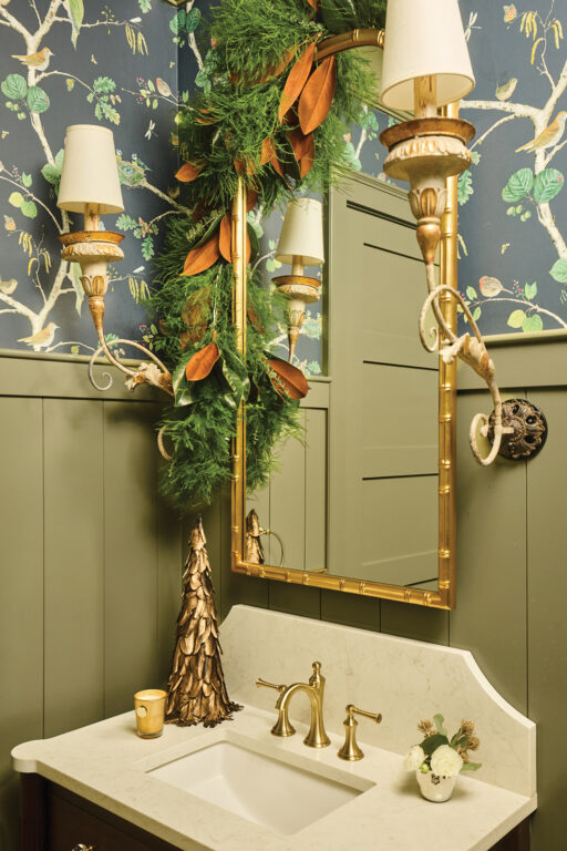 A marble sink and gold mirror in a powder room with green wainscoting and colorful nature-themed wallpaper