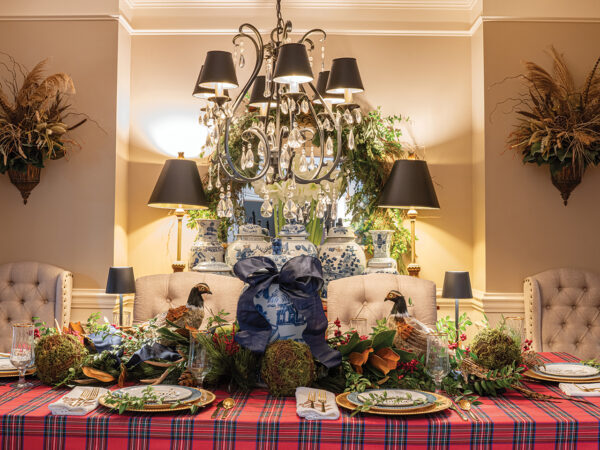 An elegant dining table with a holiday centerpiece that includes greenery and fake pheasants
