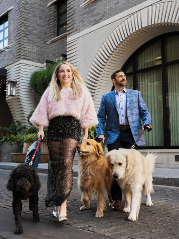 A man and woman walking two golden retrievers and a brown doodle