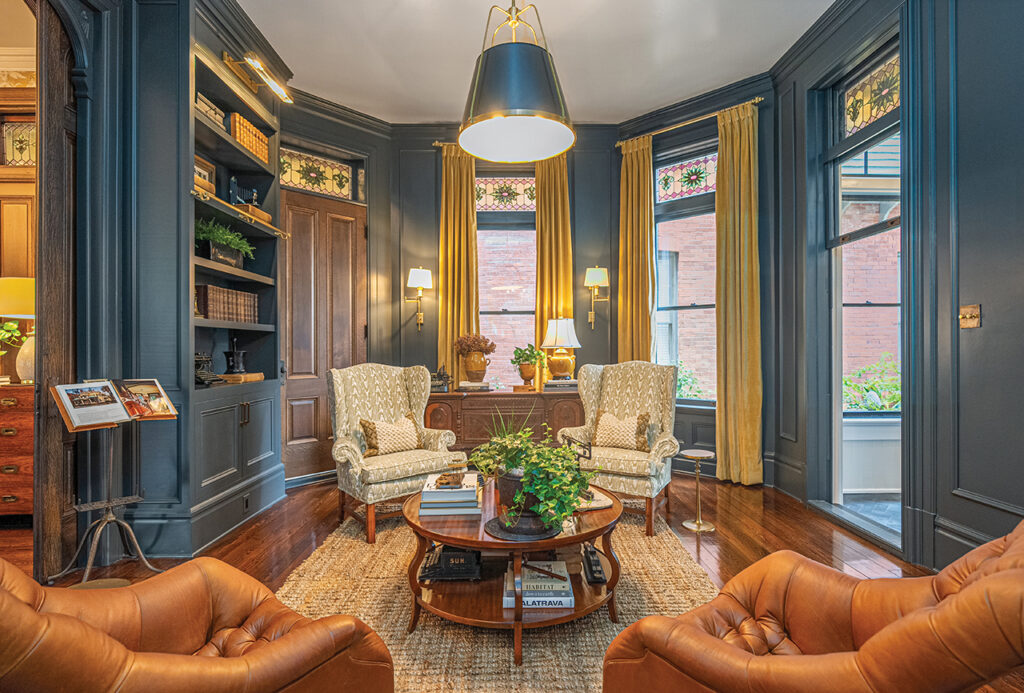 Library in a Victorian house with dark blue walls, gold curtains and camel colored leather chairs