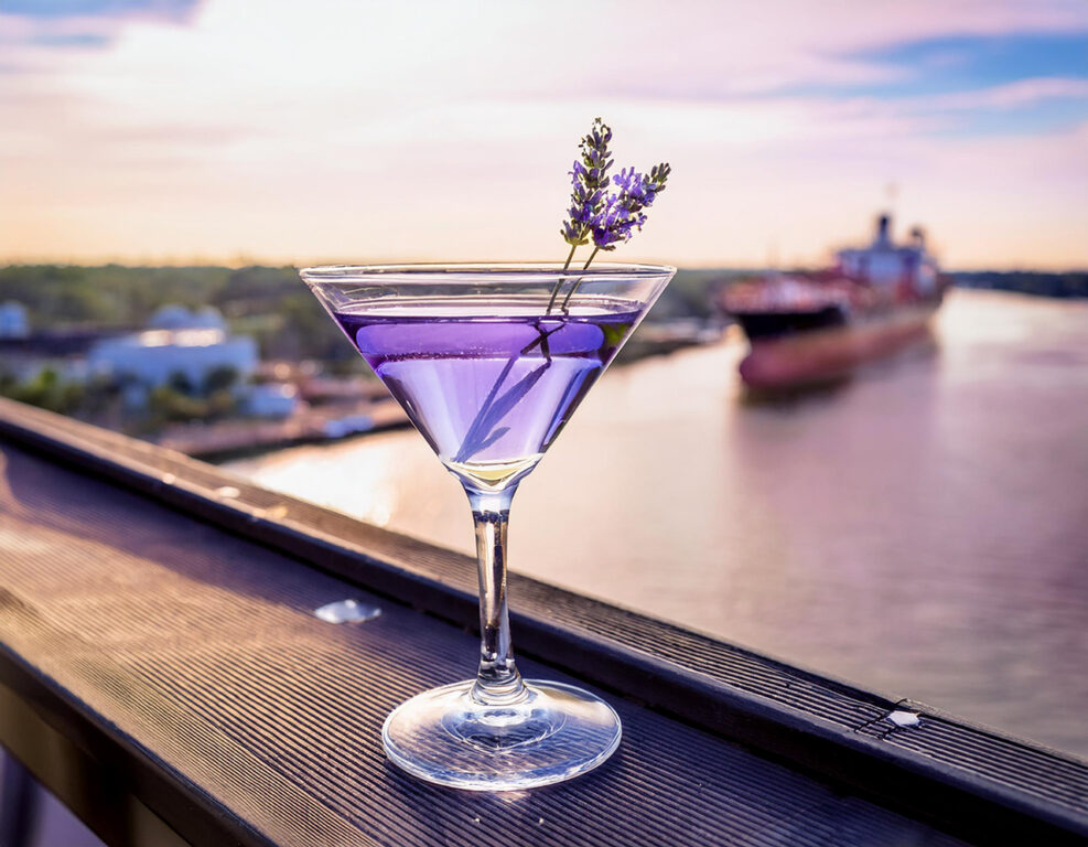 Purple lavender martini on the railing of an outdoor bar overlooking a river