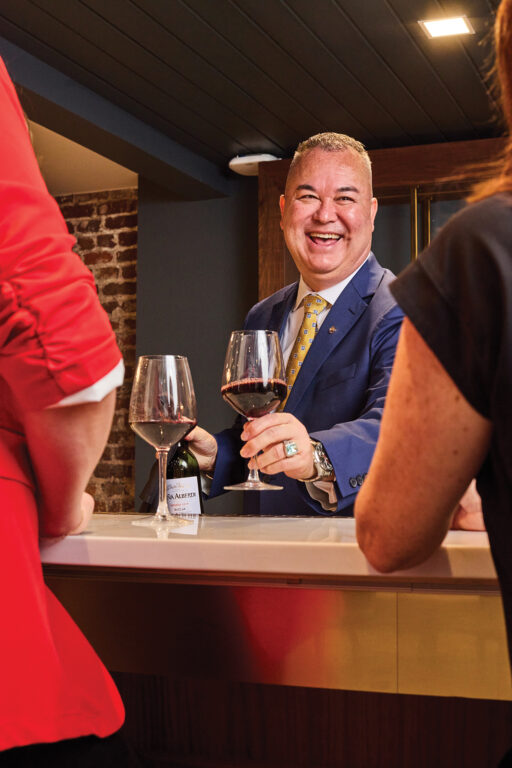 A man smiling and handing another man a glass of wine