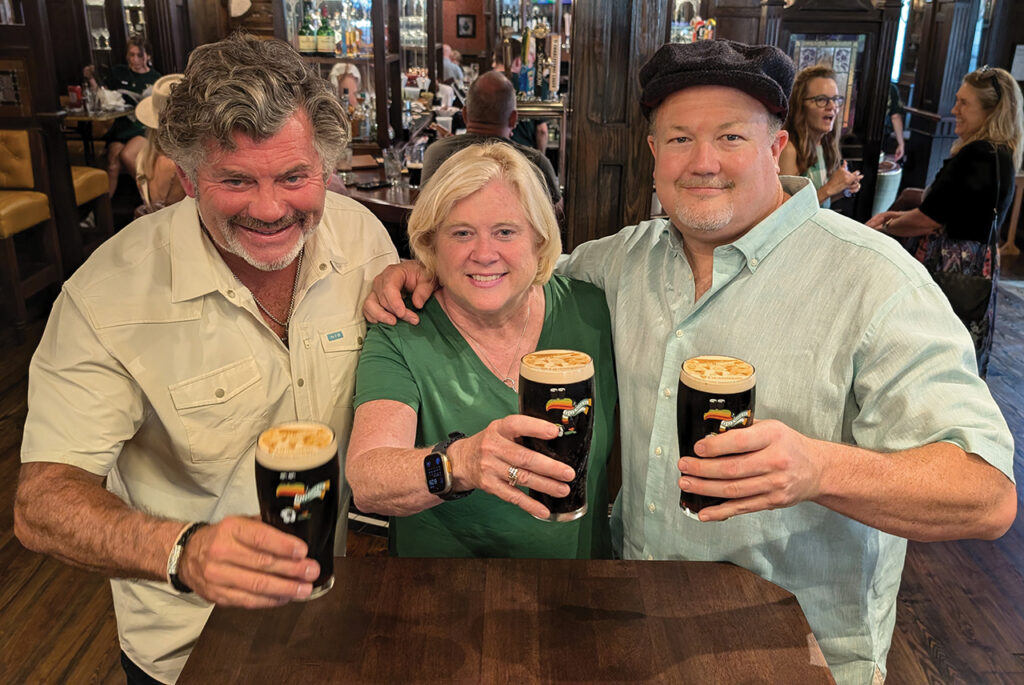 Two men and a woman holding pints of beer