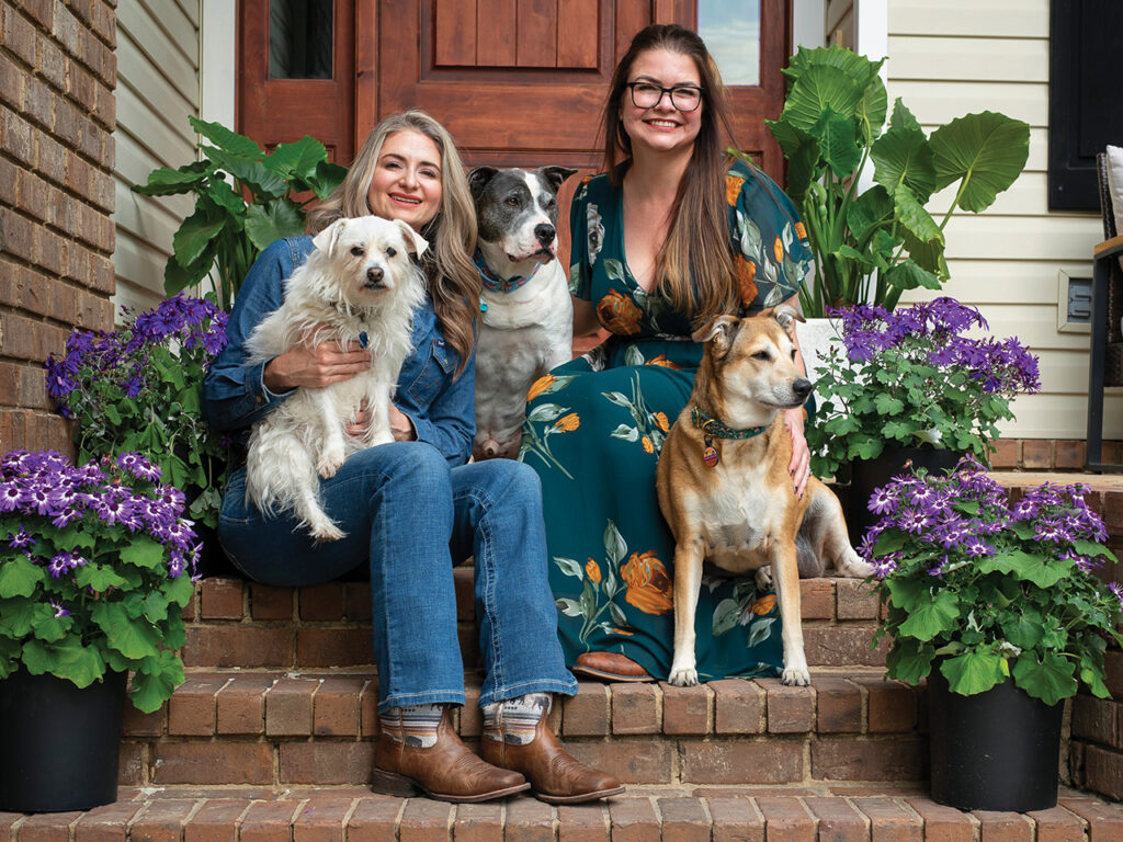 two women sitting on a home's front steps with their three dogs
