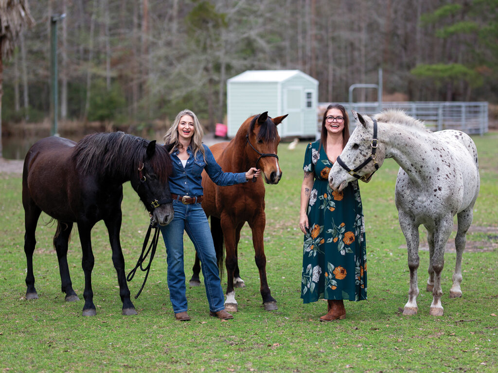 two women standing with three horses